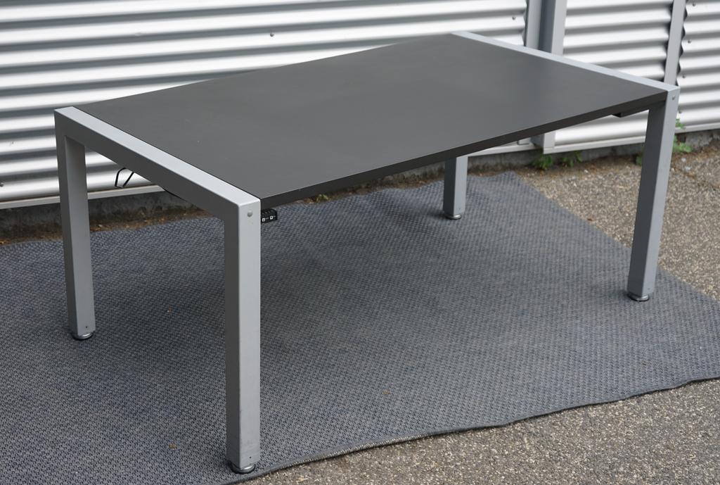 Dencon hæve-sænkebord 160x90 med sort linoleum bordplade og firbenet gråt stel set fra skrå vinkel.